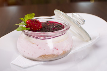 Chia pudding with granola and strawberries in a glass jar on the wooden table. Beautifully served meal at the restaurant. Tasty dessert in a beautiful decoration. 