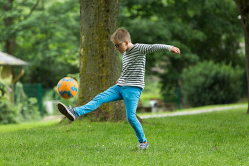 Jugendlicher / Heranwachsender / Junge / Kind spielt mit Fussball auf grüner Wiese / Wald