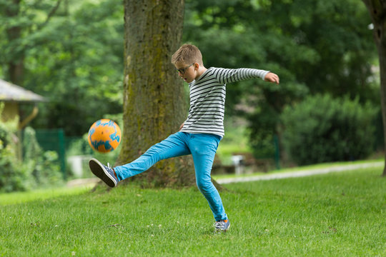 Jugendlicher / Heranwachsender / Junge / Kind spielt mit Fussball auf gr&uuml;ner Wiese / Wald