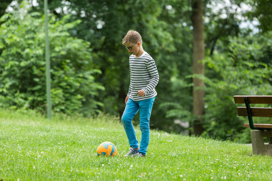 Jugendlicher / Heranwachsender / Junge / Kind spielt mit Fussball auf gr&uuml;ner Wiese / Wald