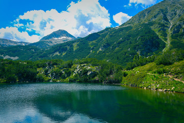 Beautiful mountains lake with a reflection of the high green mountains peaks, on the blue sky background. Amazing Mountain hiking paradise landscape with a lake, no people.