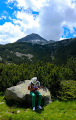 Tourist is playing on the Ukulele guitar at the mountain nature green landscape. Photo depicts romantic view of the young man playing on musical instrument in the mountains.