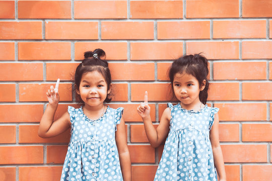 Portrait Of Two Asian Kid Girls Pointing Up On Brick Wall Background In Vintage Color Tone