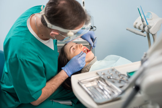 Male dentist with dental tools - mirror and probe checking up patient teeth at dental clinic office. Medicine, dentistry and health care concept. Dental equipment