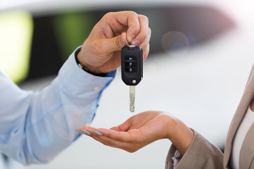 Car salesman handing car keys to woman in showroom
