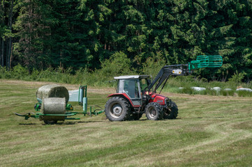 Tractor collecting a roll of haystack in the field