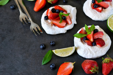 Dessert pavlov with strawberries and blueberries on a black background.
