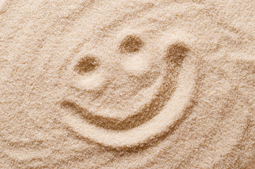 Fototapeta na wymiar Happy smiling face in the sand. Eyes and mouth drawn with a finger in dry ocherous sand. Macro photo close up from above.