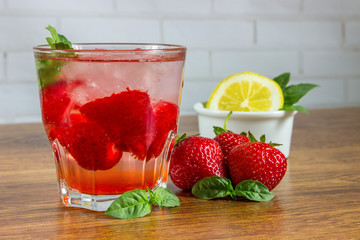 A refreshing summer drink with ice, strawberries and lemon on a wooden background. The concept of fruit drink.