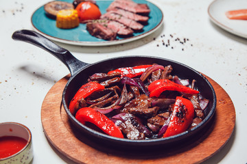 Mexican fajitos in a frying pan on a white table.