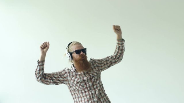 Slowmotion of Happy young bearded man in sunglasses and headphones dancing and listen music on white background