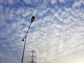 High voltage post with street light under cloudy blue sky background