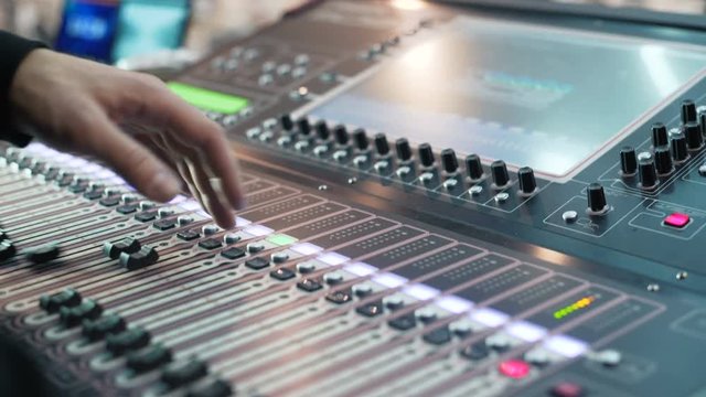 Sound director records announcer. Sliders go forward and back, multicolored buttons flash. Recording studios audio console and hand pulling up knob. DJ Workplace. Creating a sound design. Close-up DOF