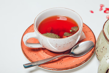 Cup of hot fruit tea on white table with mint.