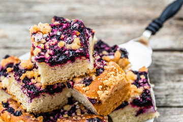 Sweet tart baked with blueberry fruits on yeast dough, pieces on plate on wooden table