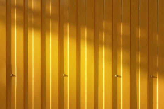 A corrugated fence of yellow metal sheets with screw. Texture of metal fence picket Profile decking. Internal primed side of a metal picket fence. Profiled metal.