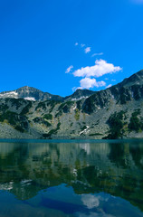 Fototapeta na wymiar Beautiful mountains lake with a reflection of the high green mountains peaks, on the blue sky background. Amazing Mountain hiking paradise landscape with a lake, no people.