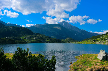 Naklejka na ściany i meble Beautiful mountains lake with a reflection of the high green mountains peaks, on the blue sky background. Amazing Mountain hiking paradise landscape with a lake, no people.