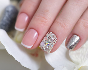 Beautiful classic French manicure with rhinestones on female hand. Close-up. Picture taken in the studio on the background of flowers