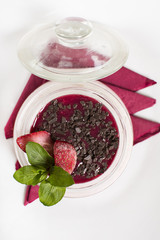 Delicious pudding with chocolate flakes and strawberries in a glass jar on the wooden table. Tiramisu in a glass cup. Close up of a delicious dessert.