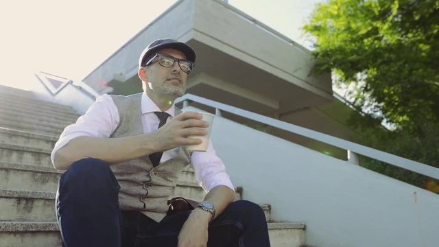 Mature businessman sitting on stairs in the city, drinking coffee.