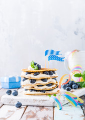 Small cake made of pancakes with cream and blueberries on old white wooden board. Children's party background. Healthy food concept, copy space.