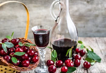 Papier Peint photo Alcool Glass of wine and vintage glass bottle on wooden table. Sweet alcohol made from cherry fruits