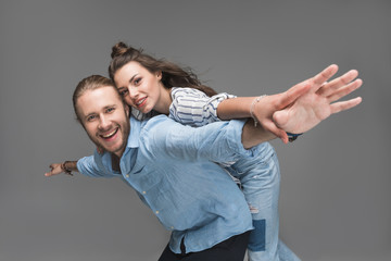 Happy young couple piggybacking and smiling at camera isolated on grey