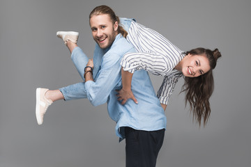 Cheerful young man carrying happy young woman and smiling at camera