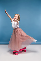 Naklejka premium Cute smiling girl in pink skirt standing on skateboard and having fun