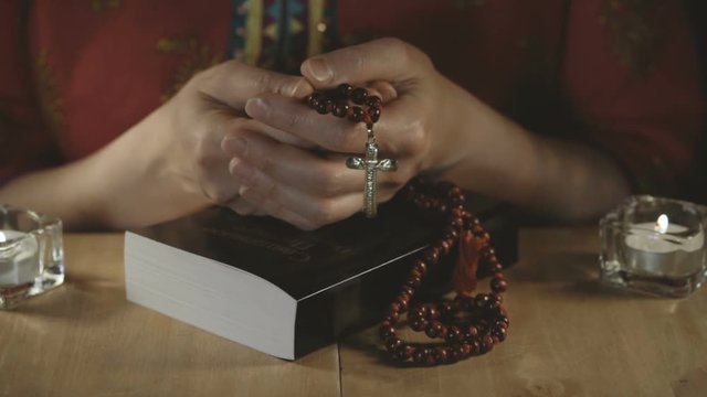 Women's hands holding a cross with rosary on a closed bible.
