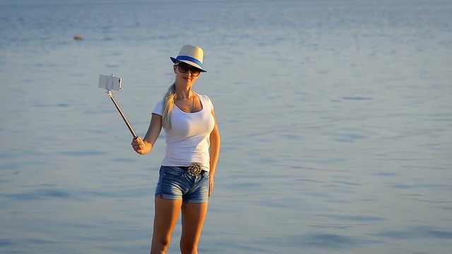 Girl tourist in short shorts does selfie on mobile phone in a trip by the sea.