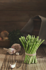 Bunch of fresh green asparagus bandaged with a rope. Fresh asparagus and vegetables on a wooden table in a rustic interior. Low key, copy space.