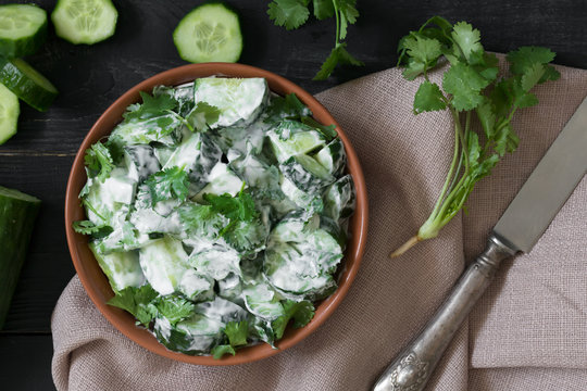 Cucumber salad with yogurt dressing on the black wooden background