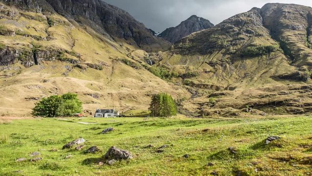 Bewegter Zeitraffer &uuml;ber den Glencoe Bergen Stob Coire Nam Beith und Beinn Maol Chaluim mit Wasserfall und wissem Haus im Hintergrund