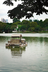 Pleasureboat on a lake in the heart of Bangkok - Lumphini Park. Business district cityscape from a park with cloudy sky in the evening with reflection.