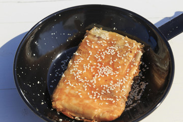 Phyllo wrapped feta cheese appetizer with honey and sesame seeds, Traditional greek dish on the white wooden table background served by the sea