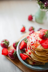Beautiful homemade pancakes with strawberry and raspberry red jam on a white brick wall background. Pancakes with fresh juicy strawberries and a vase with red flowers asters. Pancakes, top view, side 