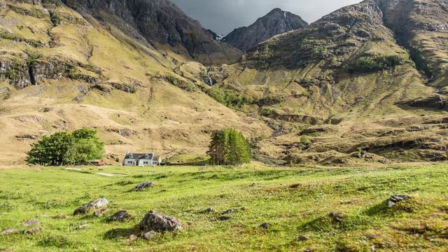 Bewegter Zeitraffer &uuml;ber den Glencoe Bergen Stob Coire Nam Beith und Beinn Maol Chaluim mit Wasserfall und wissem Haus im Hintergrund