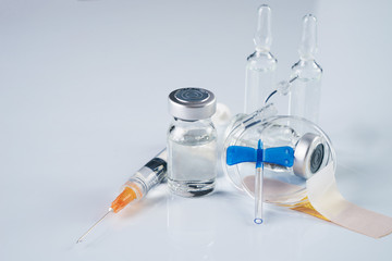 Medical ampoules, infusion and syringe with injection isolated on white background with copy space. Ampules with antibiotics closed with caps in a row. Syringe with needle lying on the vial with drug