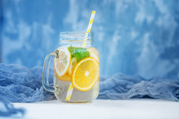 Refreshing cocktail in a glass jar. Lemon, orange and mint. Blue background. The concept is summer, diet, vegetarian, fitness, healthy eating and lifestyle.