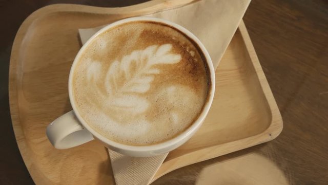 Panning shot of hot latte art coffee on wooden dish