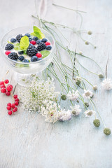 Glass plate with yogurt and various berries And wild flowers of the field on an old wooden cracked light background.
