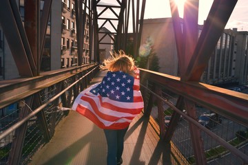 Young woman wrapped in American flag on an iron bridge at dusk of the city