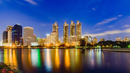 Bangkok city skyline and office buildings in twilight time with skyscrapers and lights reflecting in the lake at Benjakitti Public Park, Bangkok, Thailand.