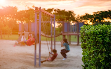 Abstract blurred motion colorful children playground activities in public park at sunset. Selective focus on bush.