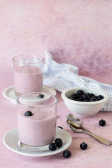  Blueberry dessert. Yogurt in a glass and fresh blueberries on a light pink background.