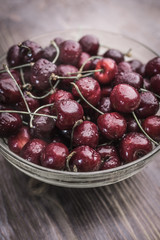 A bright ripe sweet cherry covered with cold drops of water lies in a transparent bowl on a brown wooden background