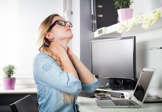 Woman in home office suffering from neck pain sitting at desk