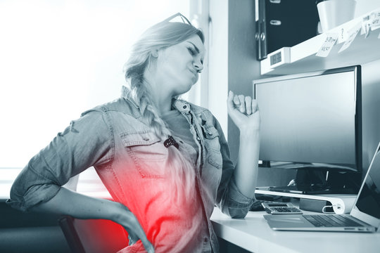 Woman in home office suffering from backache sitting at computer desk